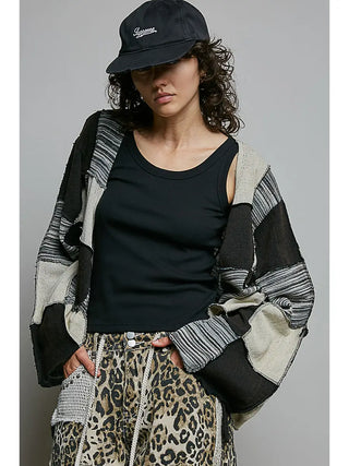 A relaxed fit cropped cardigan with a black patchwork design, worn by a model with a black cap.