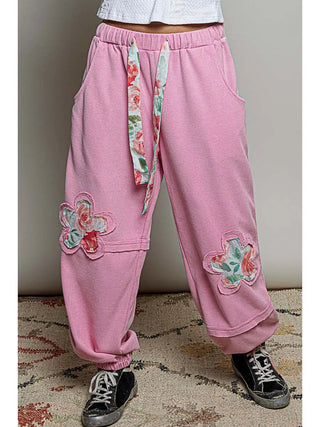 Candy pink jogger pants with floral print patches and an adjustable high-rise waist.