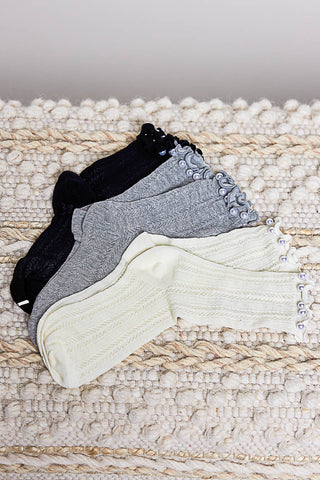 Three pairs of knit leg warmers in black, gray, and cream with decorative buttons.