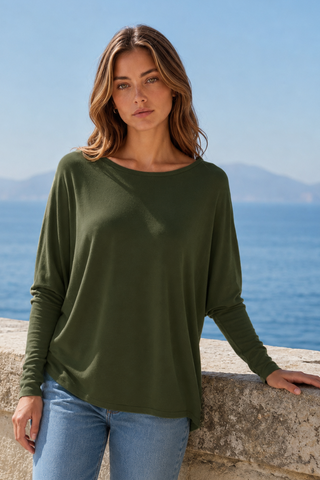 A woman wearing a relaxed fit, olive green long sleeve top with jeans, standing by the sea.