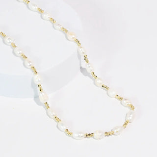 Pearl necklace with gold accents laid on a white surface.