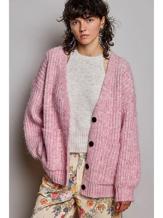A woman wearing a pink oversized ribbed knit cardigan with a V-neck and button closure.