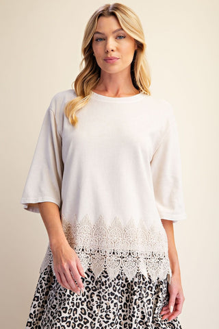 Boxy knit top in ecru with a lace trim at the bottom, worn by a model.