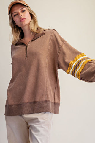Woman wearing a mocha-colored half zip pullover with contrast stripe sleeves.