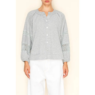 Light heather grey button-down knit blouse with crochet trim on sleeves, worn by a model with white pants.