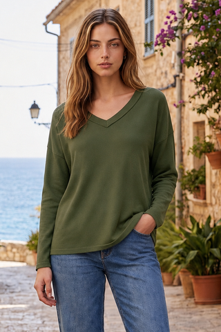 Woman wearing an olive long-sleeve V-neck top, standing outdoors with stone buildings in the background.