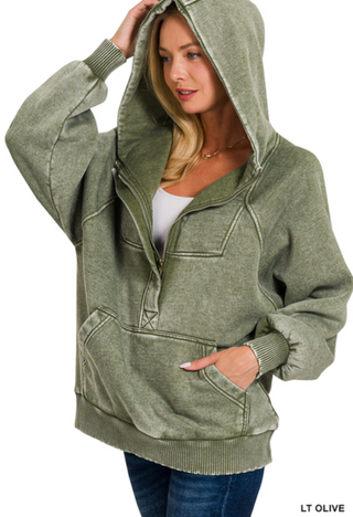 A woman wearing a light olive oversized 1/4 zip hoodie with kangaroo pocket and hood.