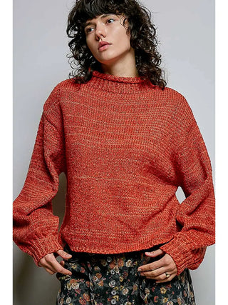A woman wearing a high-neck brick-colored sweater with balloon sleeves.