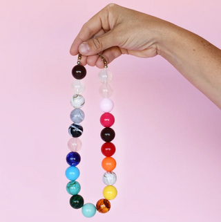 A necklace with vibrant multicolor round beads displayed against a pink background.