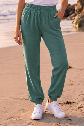 Relaxed fit joggers in hunter green with elastic waistband and cuffs, worn by a person on the beach.