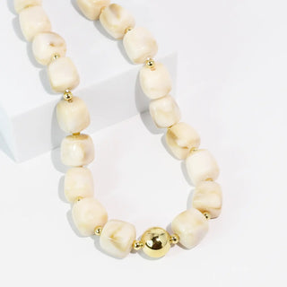 A necklace with cream-colored beads and gold accents displayed on a white background.