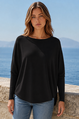 A woman wearing a black top with a relaxed fit and boat neckline, standing by the sea.