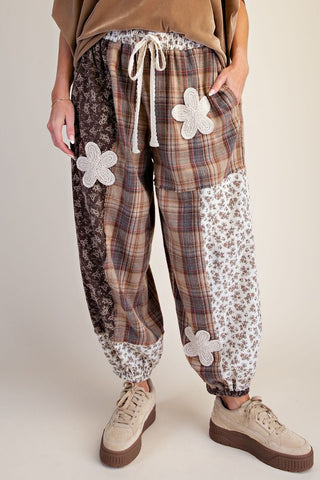 Mocha-colored pants with plaid and floral patterns, featuring drawstring waist and floral appliqué.