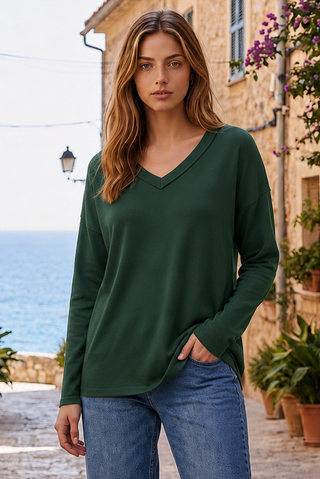 A woman wearing a hunter green V-neck top with long sleeves, paired with jeans.