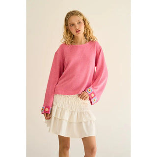 A pink knit top with embroidered cuffs, worn by a model with a white skirt.