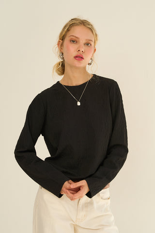 Model wearing a black long-sleeve top with textured fabric.