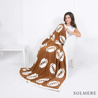A woman sitting in a chair wrapped in a brown and white football-patterned blanket.