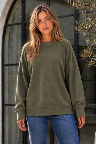 A woman wearing a relaxed fit knit sweater in forest moss with long sleeves.
