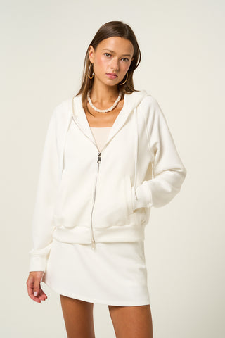White zip-up hoodie with drawstring, modeled by a woman wearing a matching skirt.