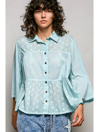 A woman wearing a textured dot woven blouse in aqua with a ruffle hem and button-down front.