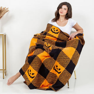 A woman wrapped in a plaid throw blanket with orange and black Jack-o'-lantern print.