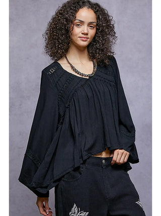 A woman wearing a black 3/4 sleeve V-neck woven top with a relaxed fit.