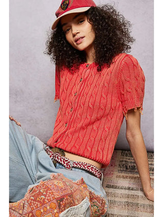 A ruby cable knit sweater top with a round neckline worn by a model.