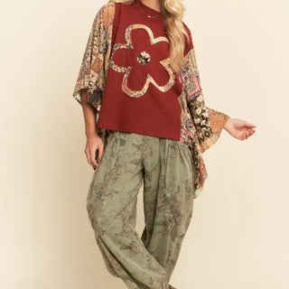 A woman wearing a burgundy knit top with a flower applique and patchwork sleeves.