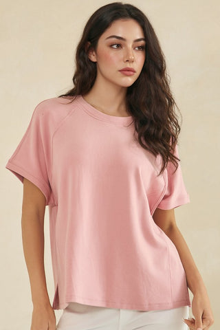 Woman wearing a relaxed crew neck tee in a soft rose color with raglan short sleeves.