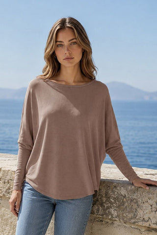 A woman wearing a mocha-colored top with long sleeves, standing by a seaside view.