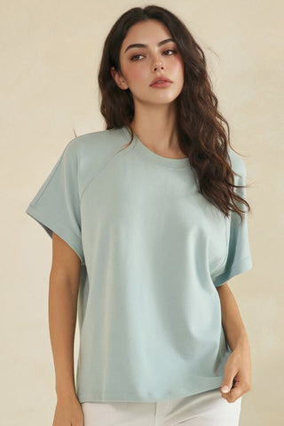 A woman wearing a light denim blue, relaxed fit, raglan short sleeve top with a crew neck.
