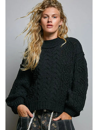 A black cable knit sweater with a mock neck and balloon sleeves worn by a model.