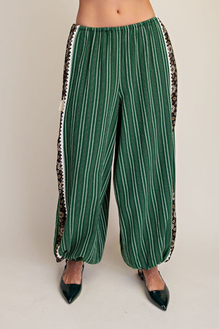 Pair of pine green woven pants with white stripes and a printed side panel.