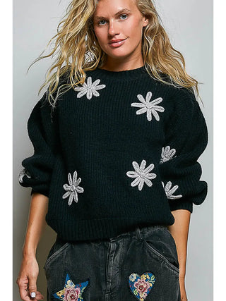 A black ribbed knit sweater with textured floral patches and a round neckline.
