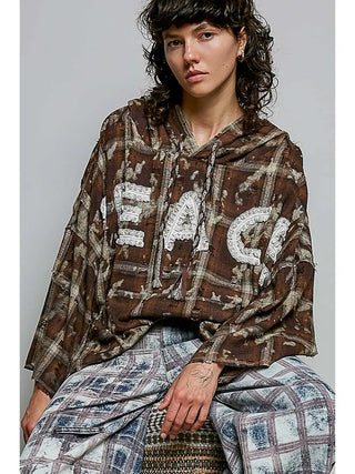 A woman wearing a choco multi plaid hoodie with lace peace letter applique and loop trim.