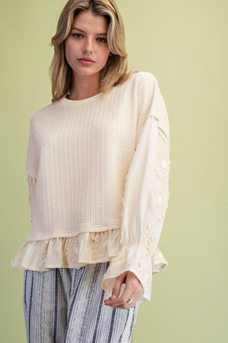 Ivory top with loose fit, ruffle bottom, and textured fabric worn by a model.