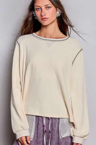 A woman wearing an almond-colored waffle knit oversized long sleeve top with a relaxed fit.