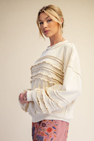 A woman wearing a relaxed-fit, ecru-colored washed terry knit tunic with ruffle details.