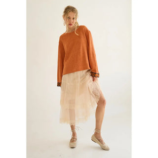 A model wearing a burnt orange knit top paired with a light, flowing skirt.