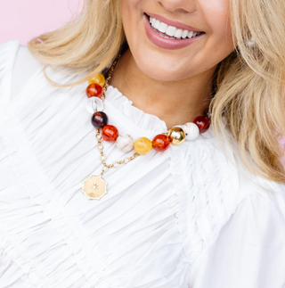 A necklace with multicolored beads and a maple pendant worn by a person in a white blouse.