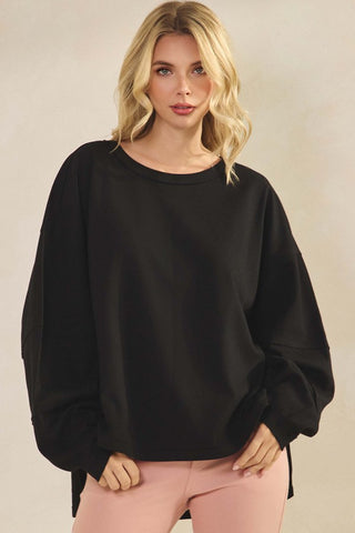 A woman wearing a relaxed fit black top with long sleeves and a round neckline.