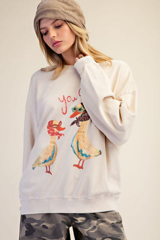 A woman wearing an ecru pullover with a graphic of two ducks on the front.