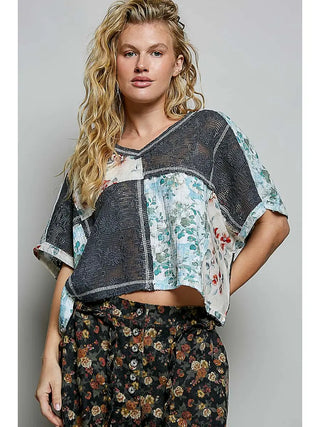 A see-through sleeveless top with a V-neck in charcoal multi print worn by a model.