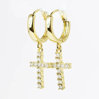 Gold huggie earrings with dangling cross charms embellished with small sparkling stones.