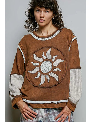 A woman wearing an espresso long sleeve top with a sun motif design made from French terry patches.