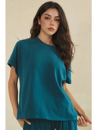 A woman wearing a teal relaxed crew neck raglan top with short sleeves.