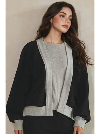 A woman wearing a black open front jacket with a grey trim over a grey top.