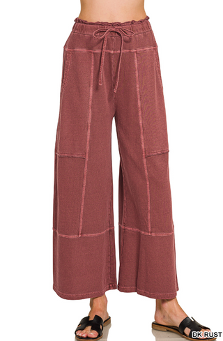 Wide leg pants in dark rust with exposed seams and a drawstring waist, shown on a model.