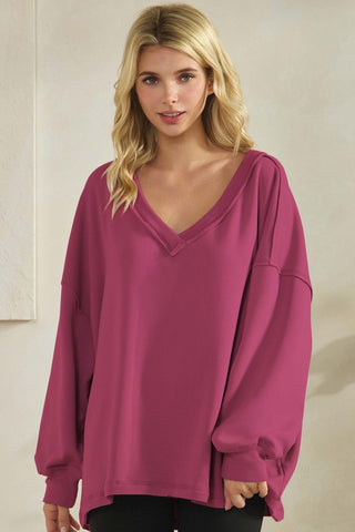 Woman wearing a loose fit V-neck top in a vibrant DRO color with long sleeves.