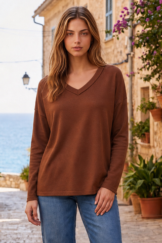 A woman wearing a caramel V-neck sweater with long sleeves, standing in a picturesque outdoor setting.